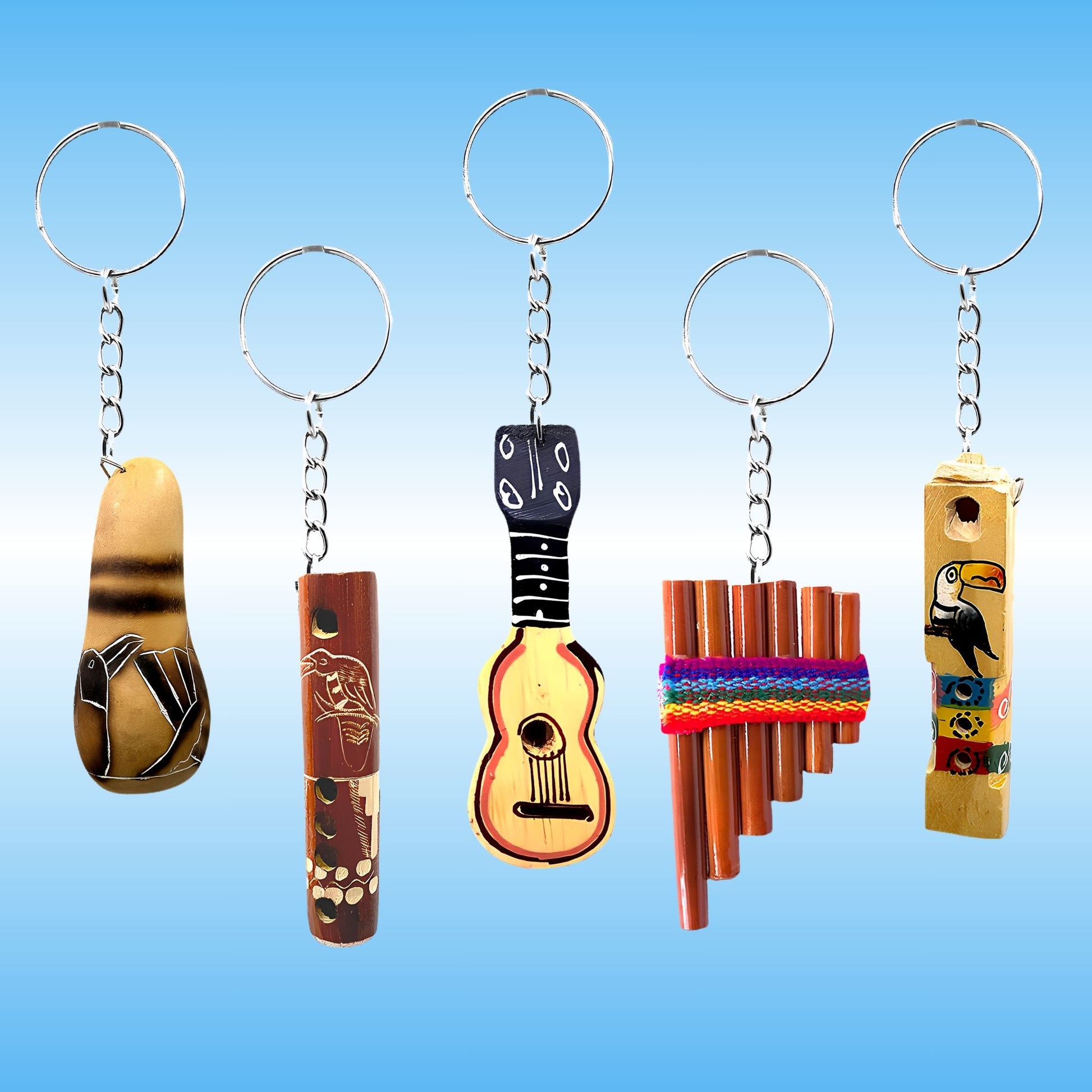 Five miniature musical instrument keychains displayed side-by-side against a light blue gradient background. The keychains include a tan and black bird-shaped flute, a brown flute with animal carvings, a yellow and black guitar-shaped whistle, a pan flute wrapped in a colorful woven band, and a yellow toucan-shaped flute with painted details.
