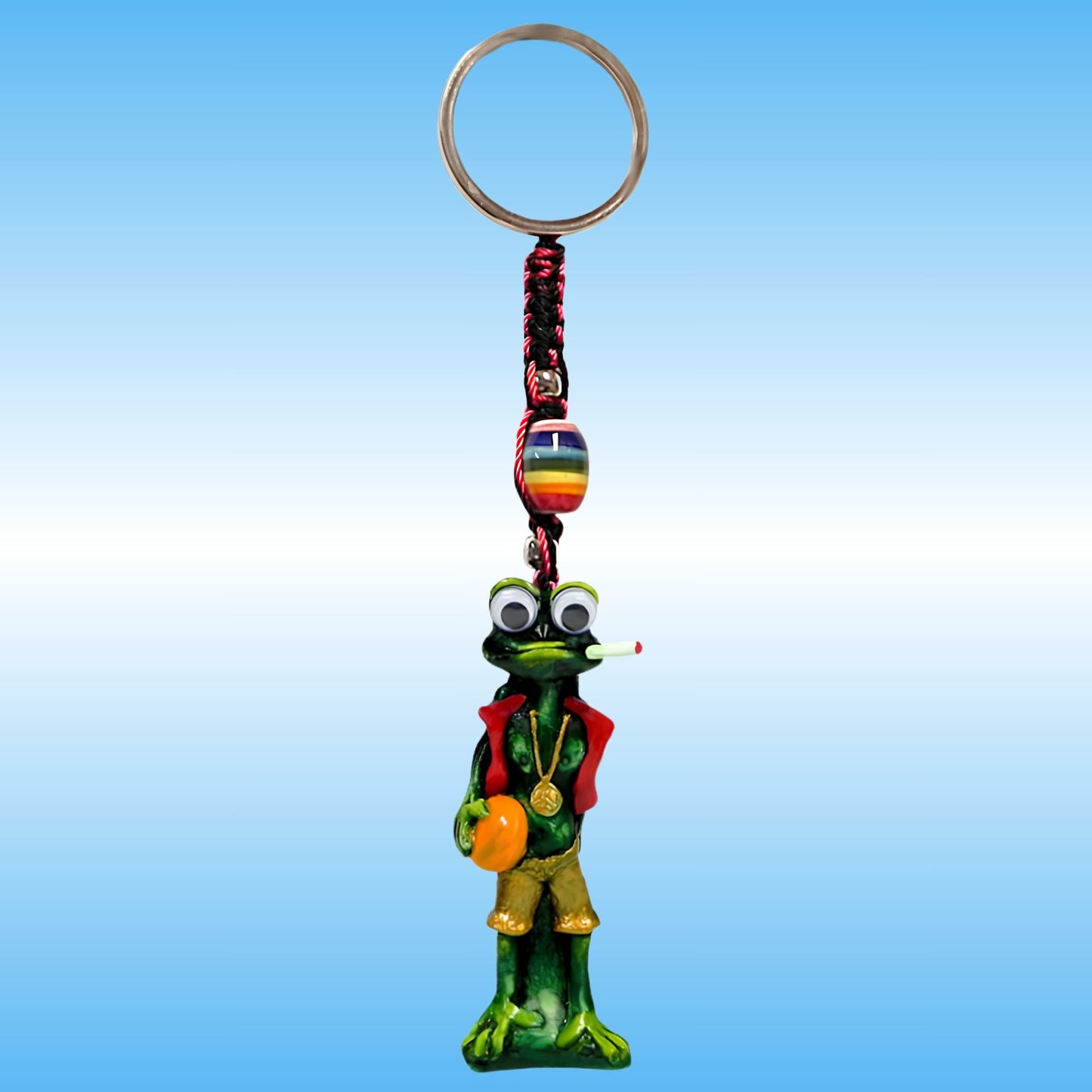 A colorful frog-shaped keychain charm with a metal key ring, black braided cord, and a striped bead, shown against a blue gradient background.