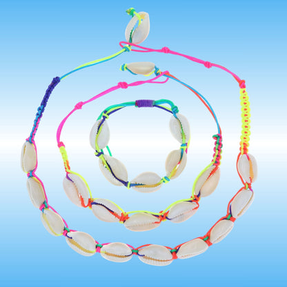 A set of three jewelry pieces made of natural cowrie shells threaded on bright neon multicolored cords, displayed on a light blue gradient background.