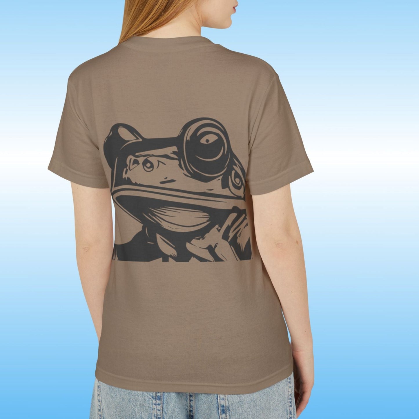 Lady  wearing a brown t-shirt with a frog graphic on the back against a blue gradient background Paddle Frogs Earthy T-Shirt Collection featuring the Frog face on the backside
