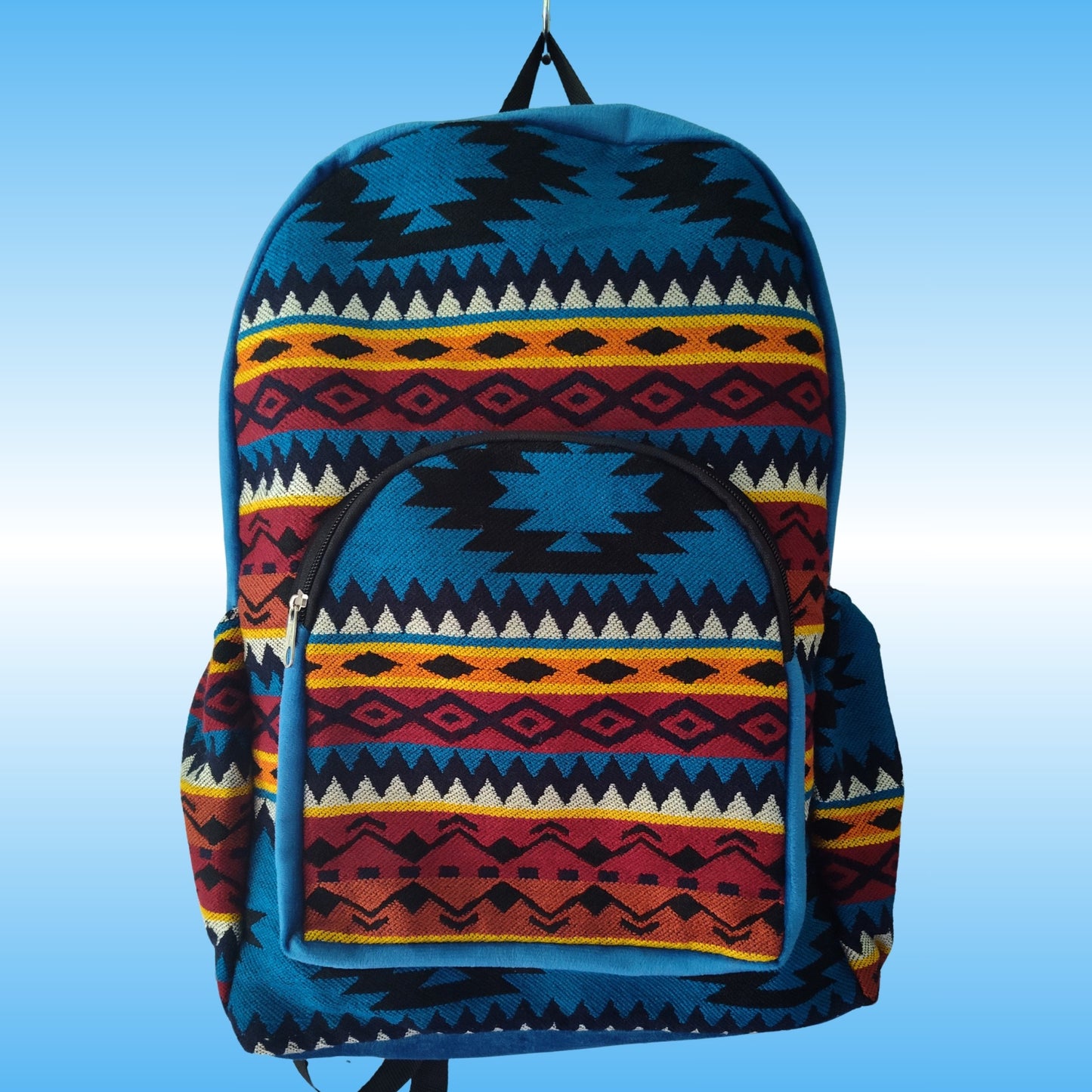A backpack with a Southwestern geometric pattern in blue, red, yellow, black, and white, shown against a light blue gradient background.