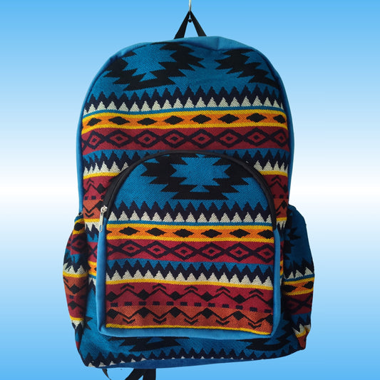 A backpack with a Southwestern geometric pattern in blue, red, yellow, black, and white, shown against a light blue gradient background.