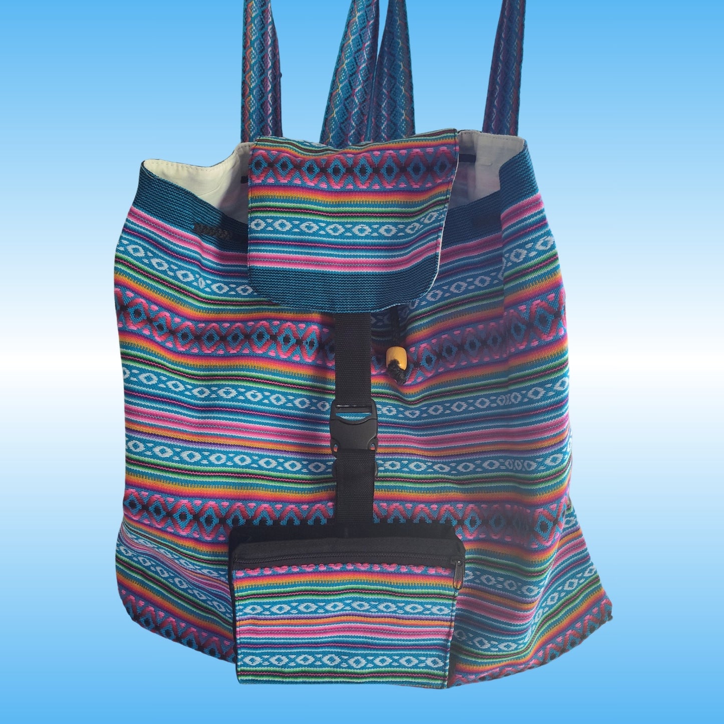 A colorful woven Peruvian backpack with a geometric multicolor pattern, featuring a front pocket and a black buckle strap closure, set against a light blue gradient background.