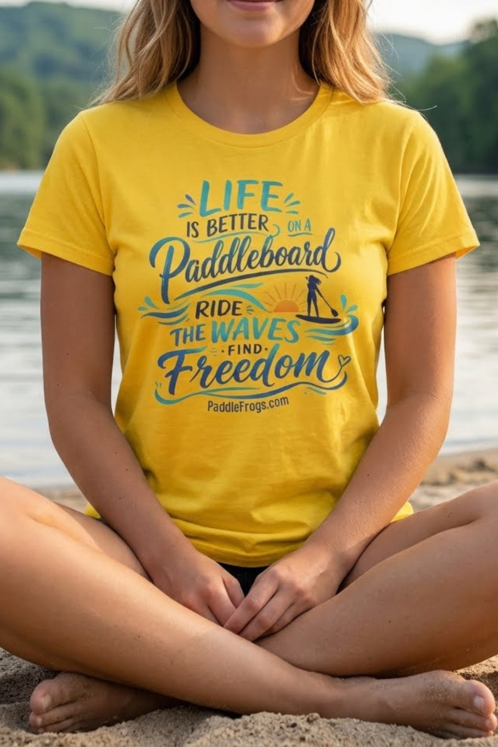 Life Is Better on a Paddleboard Women’s Tee | Paddle Frogs™ Daisy yellow color warn by a model sitting crisscross applesauce in sand beside the Emory River in Tennessee.