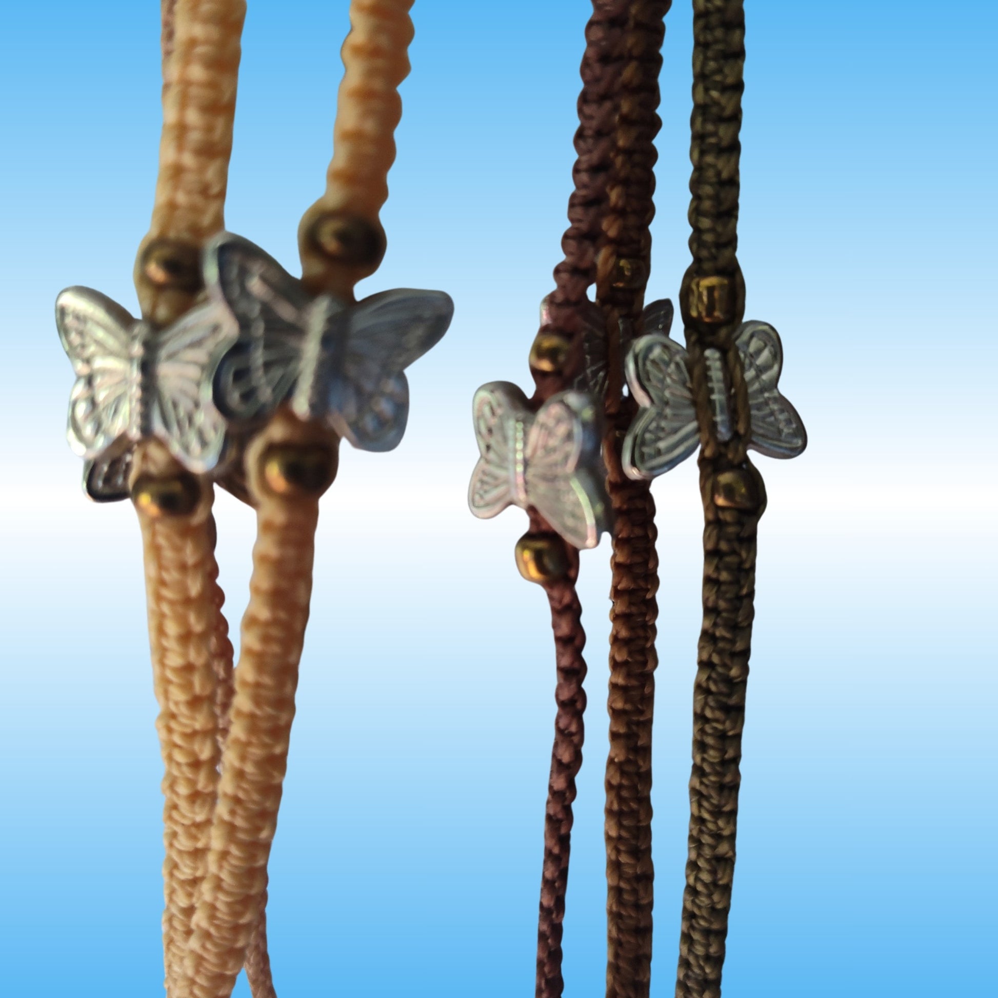 Braided cord bracelets with metallic butterfly charms and small gold-toned beads, shown against a soft blue gradient background.