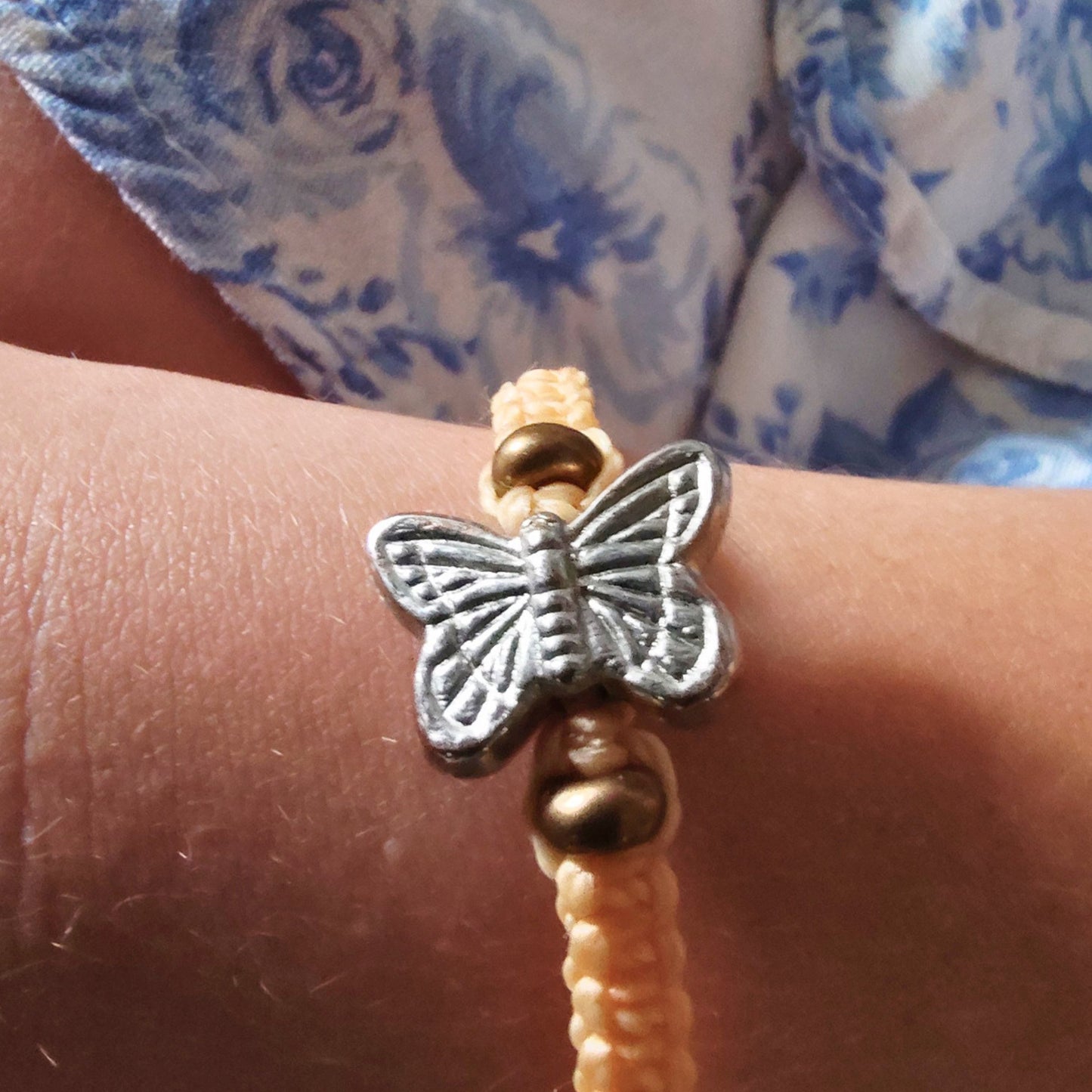 Butterfly charm friendship bracelet on a wrist with gold beads on each side.