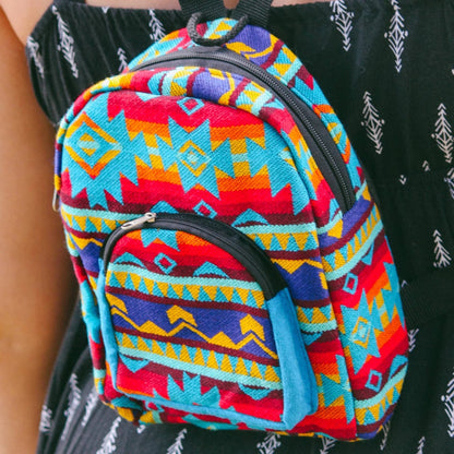 A small backpack with a colorful Southwestern geometric pattern in red, blue, yellow, and orange, worn by a person wearing a black patterned top.