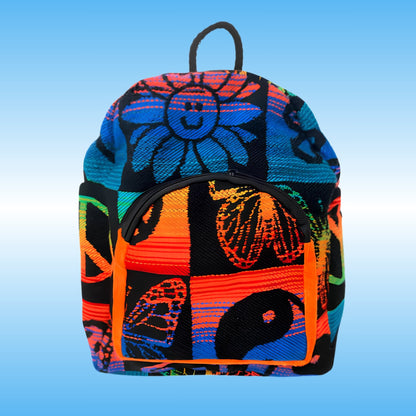 A vibrant, multicolored backpack with a patchwork design featuring a smiling sunflower, butterflies, and abstract patterns in neon orange, blue, pink, green, and black, set against a light blue gradient background.