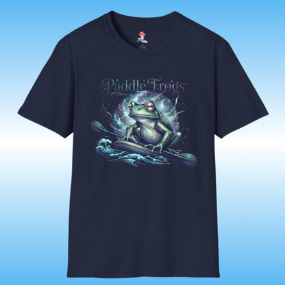 A navy blue short-sleeve t-shirt with a graphic of a green frog paddleboarding on stylized water waves, with the text 'Paddle Frogs' above. The shirt is displayed against a blue gradient background.