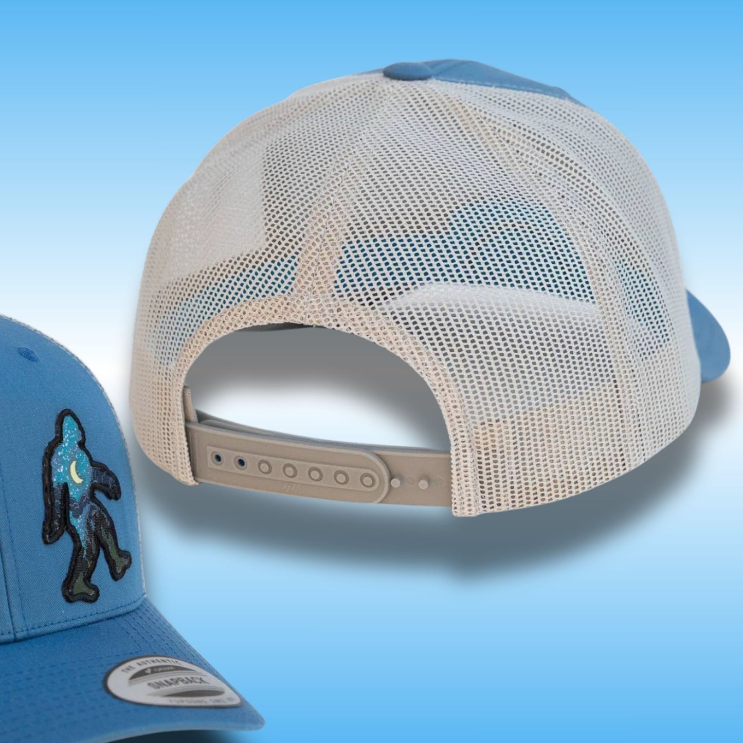 A light blue and silver trucker cap shown from the back, with a smaller inset view of the front-left corner displaying a black embroidered Bigfoot patch on a blue fabric. The cap features a cream mesh back and a light blue structured front and visor.