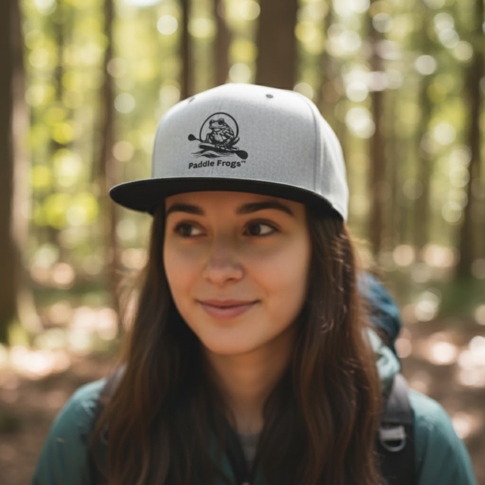 Person wearing a cap with 'Paddle Frogs' logo hiking in a forest setting