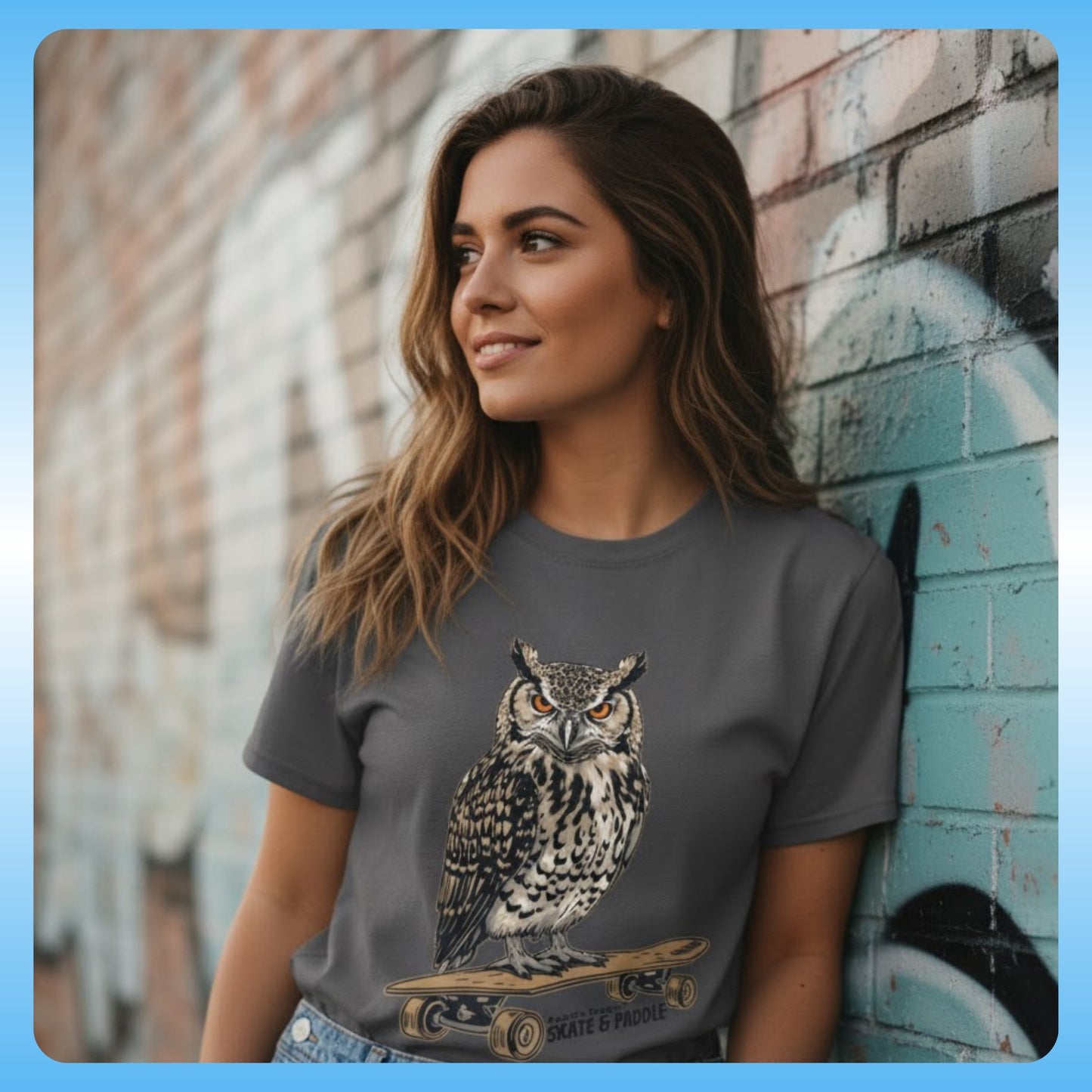 Woman wearing a gray t-shirt with an owl graphic against a graffiti-covered wall - Owl Skate & Paddle Tee - Paddle Frogs™ Outdoor Gear pro skate & paddle board shop - photography with model