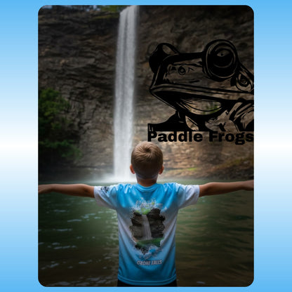 Person wearing a blue t-shirt with a frog design in front of a waterfall, featuring 'Paddle Frogs' branding. at Ozone Falls in Tennessee