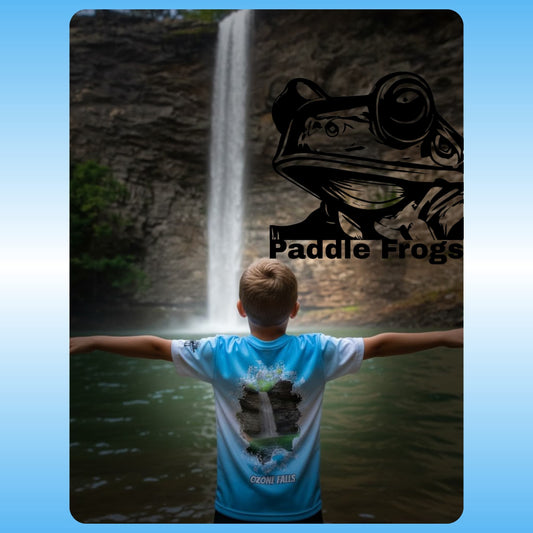 Person wearing a blue t-shirt with a frog design in front of a waterfall, featuring 'Paddle Frogs' branding. at Ozone Falls in Tennessee