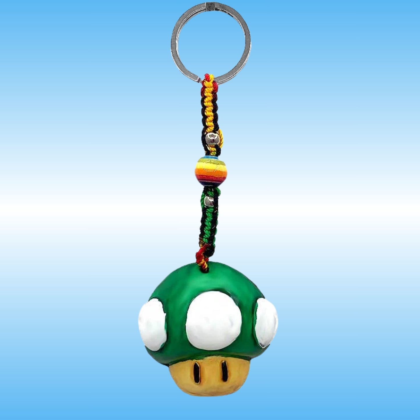 A Super Mushroom keychain featuring a green plastic mushroom with white spots and a gold mouth, attached to a braided cord with red, yellow, and green threads, a striped bead, and a silver metal key ring, set against a blue gradient background.