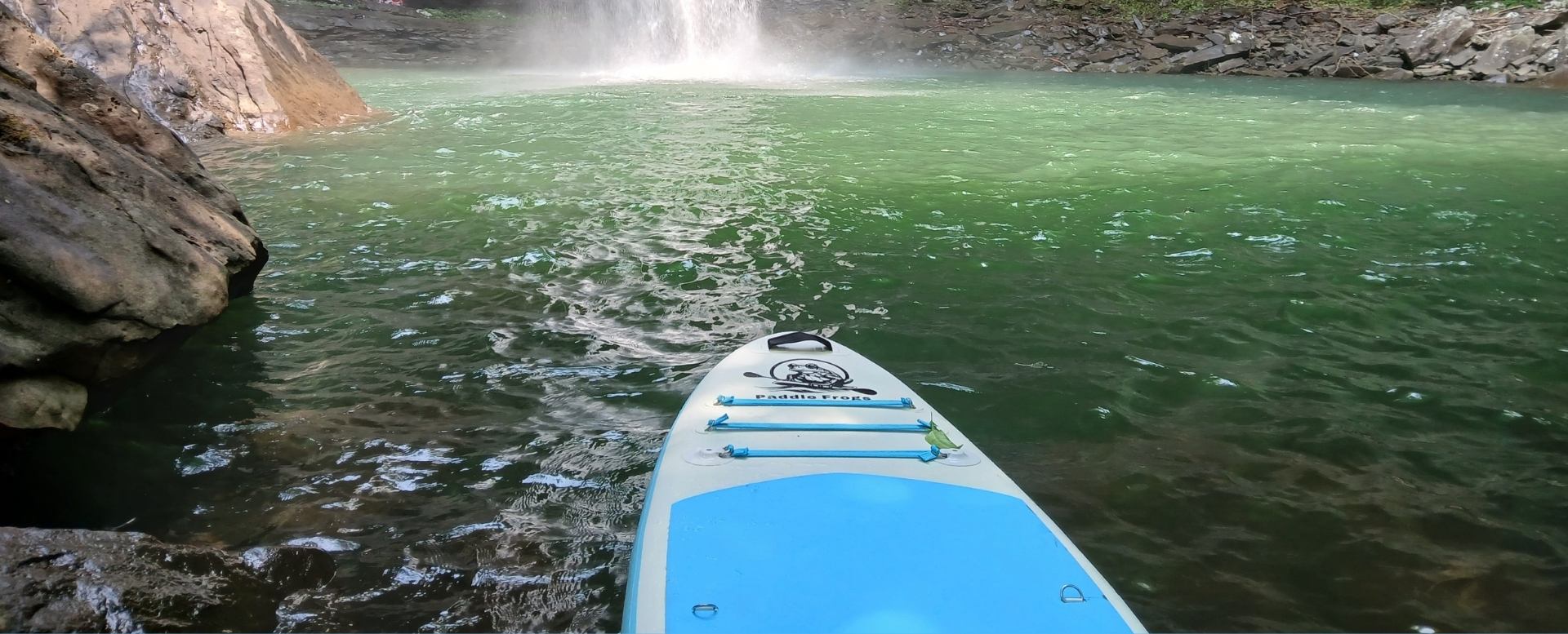 Paddle Frogs Divine Escape Paddleboard on a body of water with a waterfall in the background