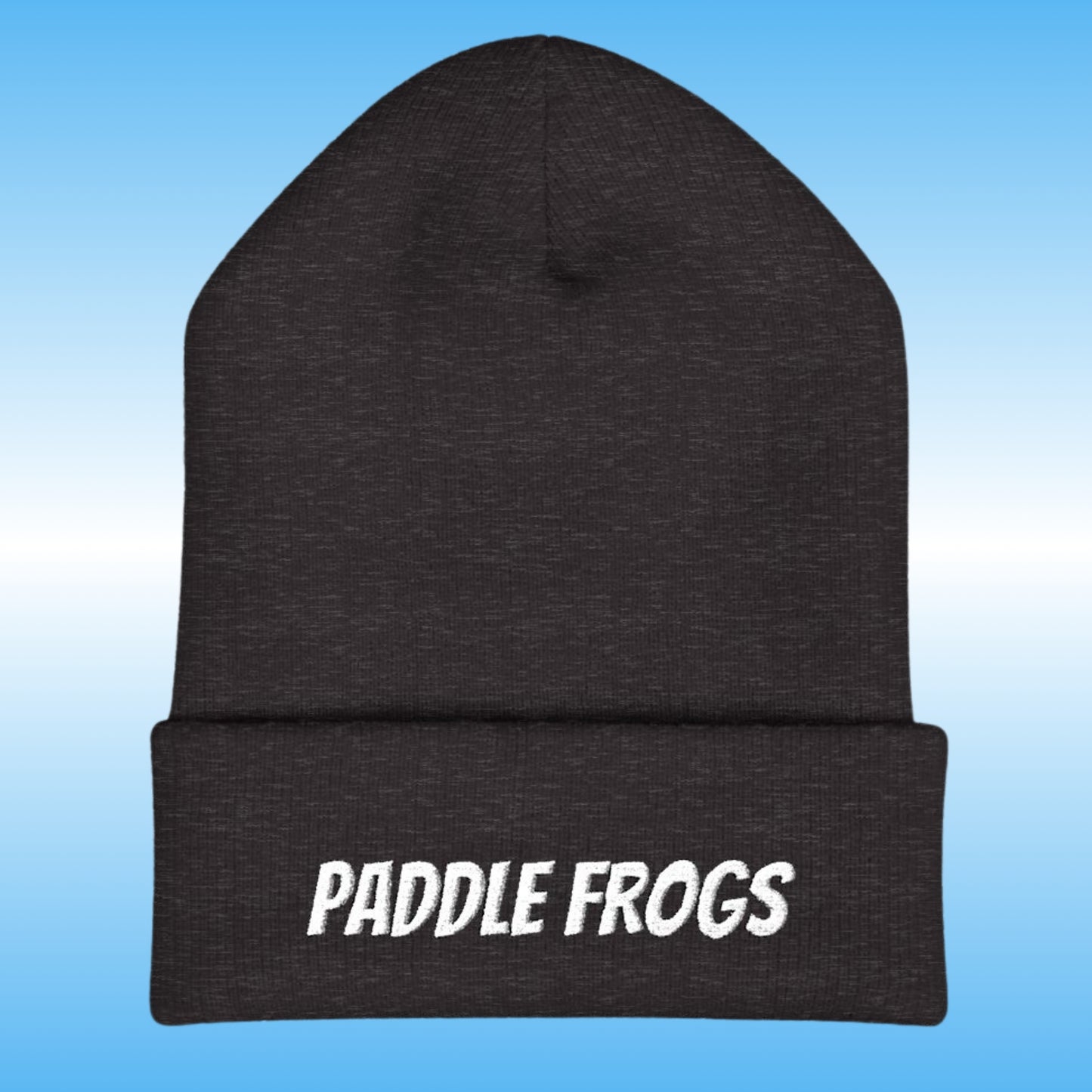 A dark charcoal gray heather knit beanie with a folded cuff featuring the words 'PADDLE FROGS' embroidered in white. The beanie is centered against a light blue gradient background.