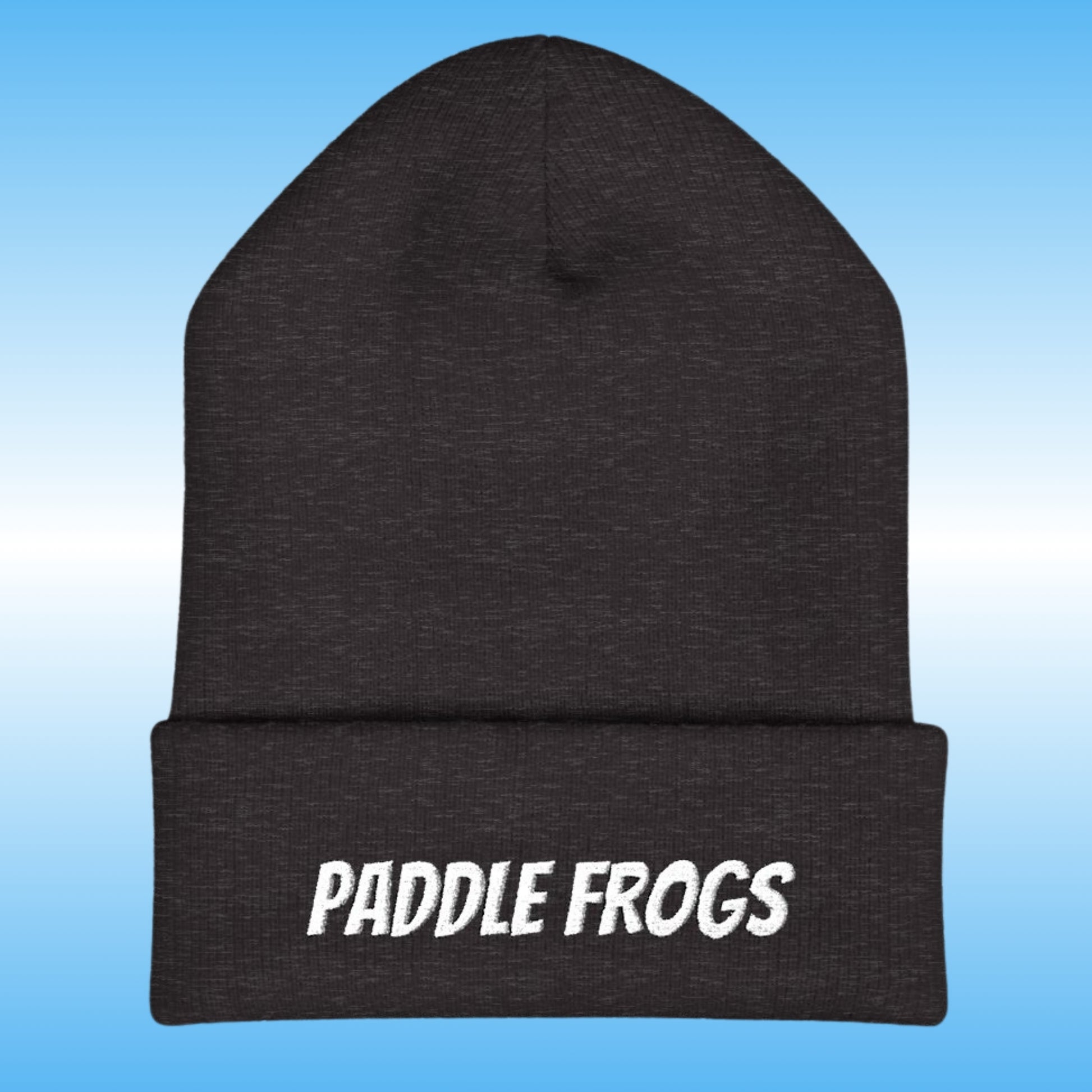 A dark charcoal gray heather knit beanie with a folded cuff featuring the words 'PADDLE FROGS' embroidered in white. The beanie is centered against a light blue gradient background.