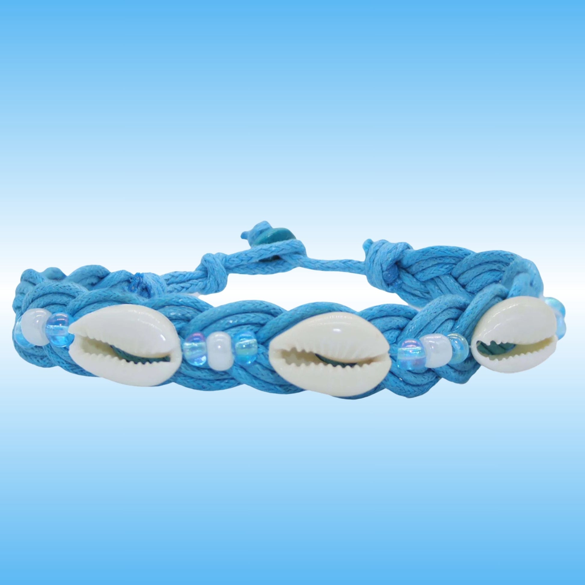 A light blue braided cord bracelet featuring three white cowrie shells and small iridescent beads, displayed against a blue gradient background.