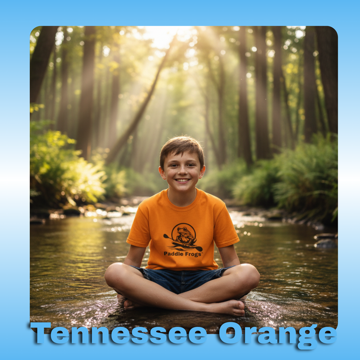 Paddle Frogs Kids T-Shirts | Tennessee Orange with an 11 year old boy in the creek | Child sitting in a stream with sunlight filtering through trees, wearing an orange shirt with 'Paddle Frogs' logo.