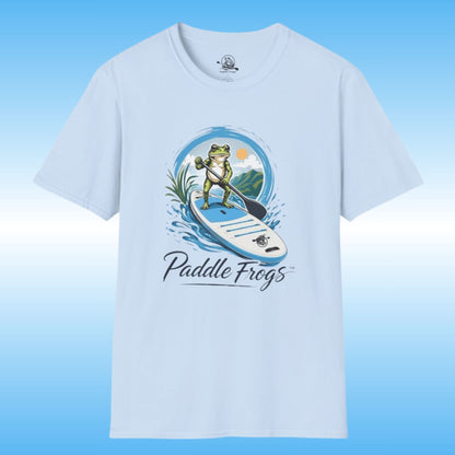 A light blue short-sleeve crewneck t-shirt featuring a graphic of a green frog paddleboarding on a SUP with the text 'Paddle Frogs' underneath, set against a blue gradient background.