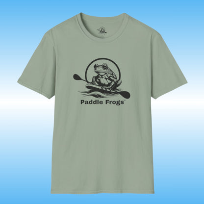 A sage green crewneck t-shirt featuring a black graphic of a frog on a paddle board with the text 'Paddle Frogs' printed on the chest, set against a blue gradient background.