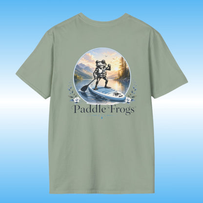 A sage green crewneck t-shirt featuring a circular graphic of a frog paddleboarding on a lake surrounded by mountains and trees, with the text 'Paddle Frogs' printed below the circle.