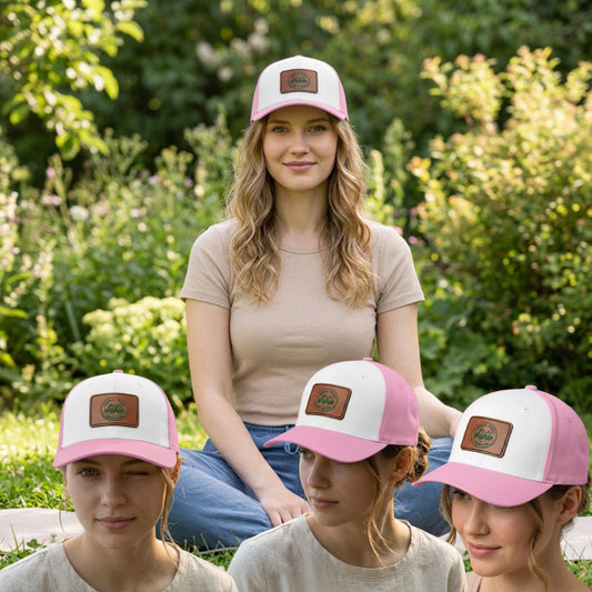 A woman and three girls wearing matching pink and white trucker hats with a brown leather patch logo, sitting outdoors in a garden setting.