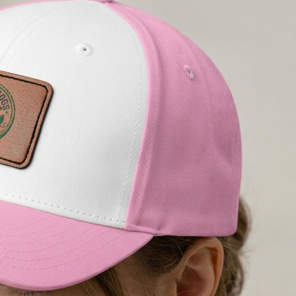 A close-up of a two-tone pink and white baseball cap with a brown faux-leather patch on the side, worn by a lady.