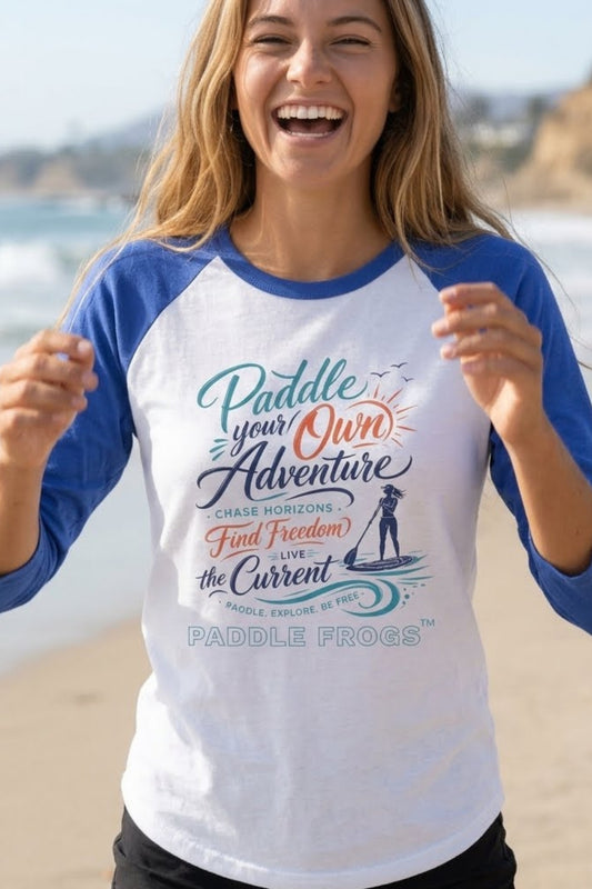 Gen z lady laughing at the beach in California. She is wearing Paddle Your Own Adventure Women’s Raglan | Paddle Frogs™ kayaking and paddleboarding White with blue sleaves tee.