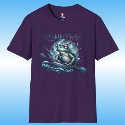 A dark purple short-sleeve t-shirt with a graphic of a green frog on a paddle board boat on stylized water waves, with the text 'Paddle Frogs' above it. The shirt is displayed against a blue gradient background.