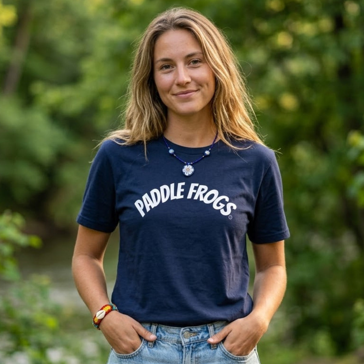 A woman wearing a navy blue t-shirt with 'PADDLE FROGS' printed in white across the chest, standing outdoors with a blurred green background.