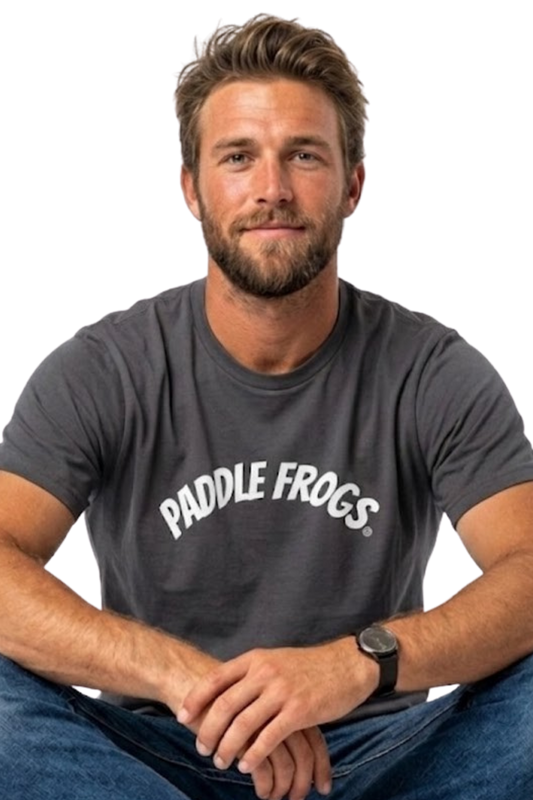 A man wearing a charcoal gray soft cotton t-shirt with 'PADDLE FROGS' printed in white across the chest, paired with blue jeans, sitting against transparent background