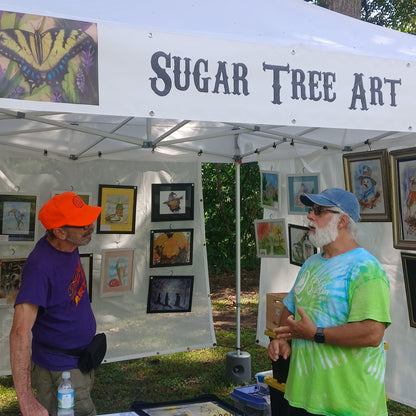 SUGAR TREE ART set up riverside and Paddle Frogs Sunday Market in Harriman, TN. He displays several framed colorful art prints ready for you to take home.