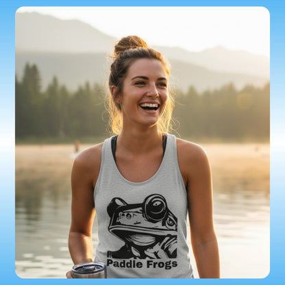 The Frog Face | Ladies Heather Gray Tank Top | Paddle Frogs - Woman wearing a tank top with a frog graphic and 'Paddle Frogs' text by a lake.