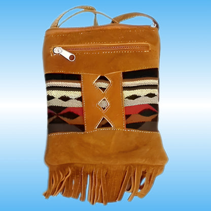A tan leather crossbody bag with a Southwestern-style woven pattern panel on the front, featuring geometric stripes in black, white, red, and brown, and a fringed bottom edge.