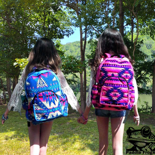 Two people holding hands with colorful patterned backpacks in a forest setting walking toward the Emory River at Paddle Frogs agritourism shop.