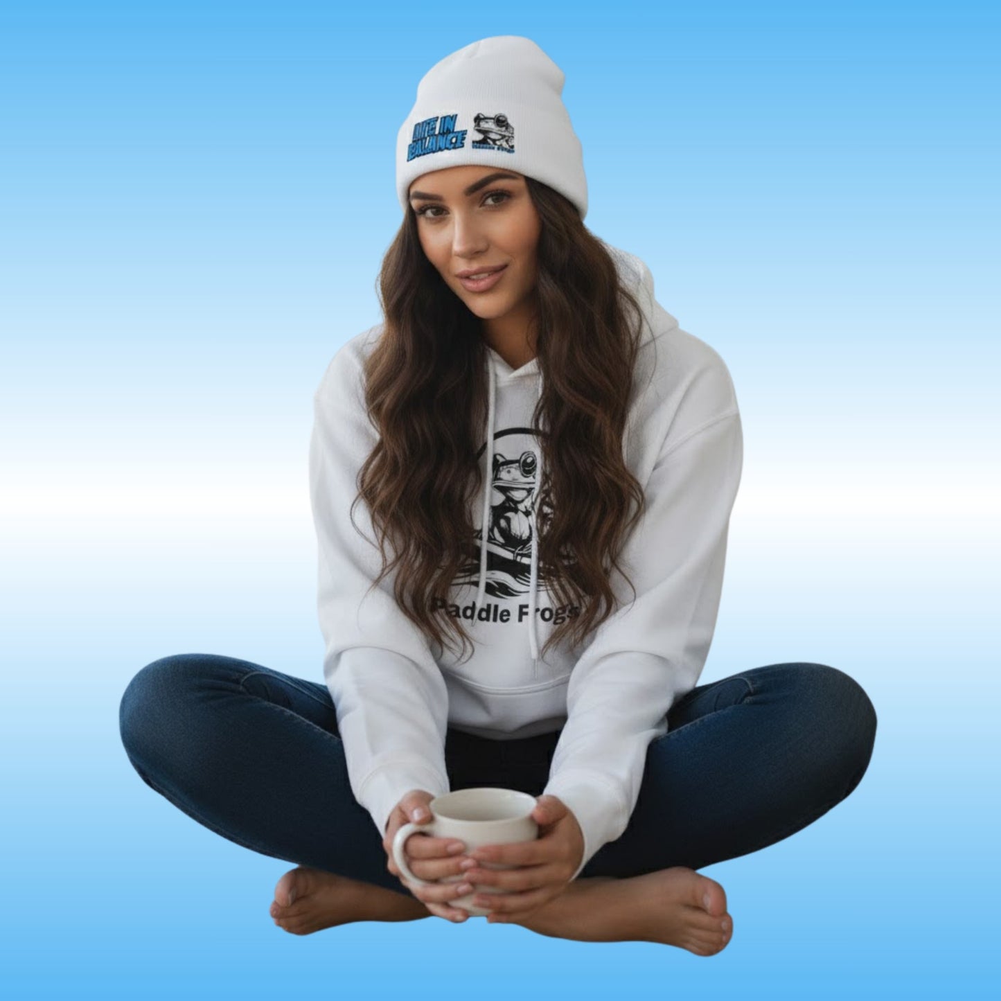 Paddle Frogs crew sitting cross-legged holding a mug, wearing a white hoodie and beanie on a blue gradient background