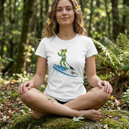 A young woman with flowers in her hair sits crisscross applesauce. She is wearing a white tee by Paddle Frogs with a lady frog on a blue paddleboard.