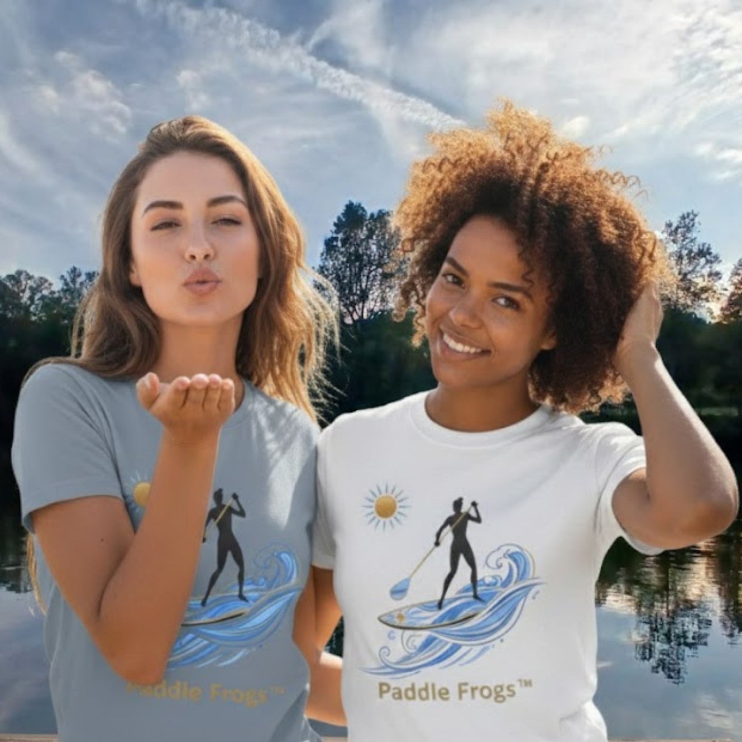 Two women wearing t-shirts with paddleboarding designs by Paddle Frogs, standing outdoors near a lake.