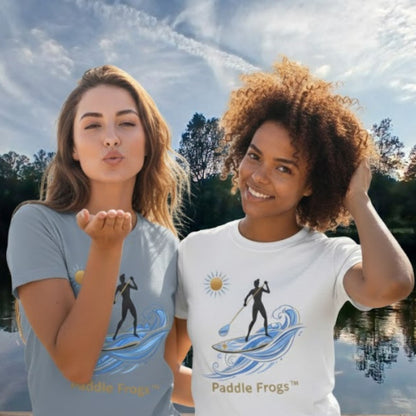Two women wearing t-shirts with paddleboarding designs by Paddle Frogs, standing outdoors near a lake.