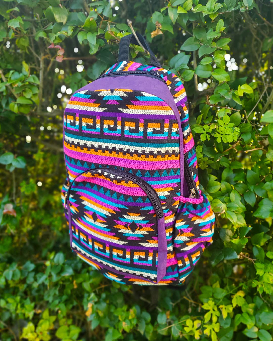 Colorful patterned backpack against a green leafy background