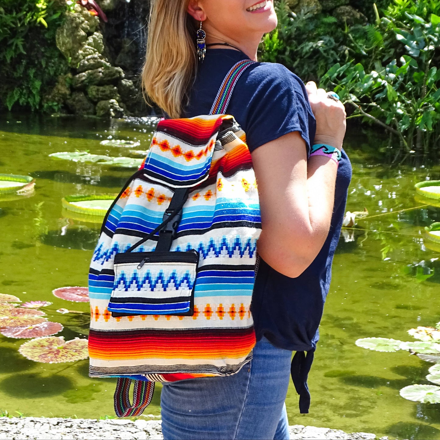 Woman with a colorful backpack standing by a pond with lily pads