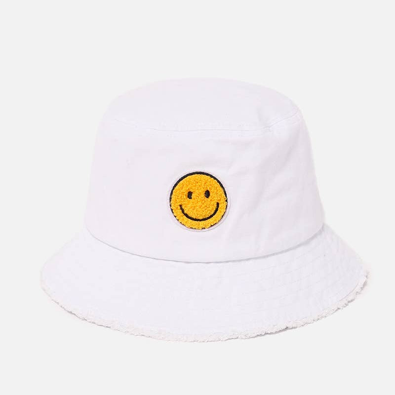 A white bucket hat with a yellow embroidered smiley face patch on the front, set against a light gray background.
