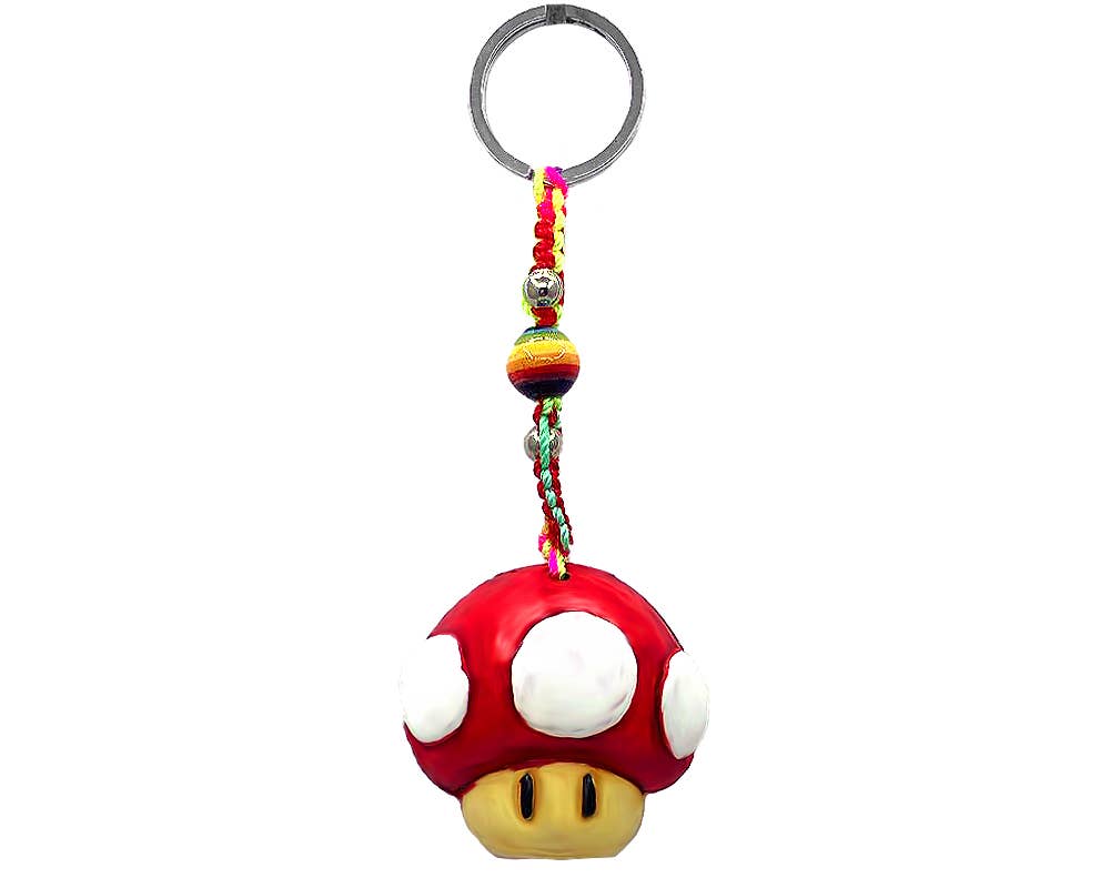 A Super Mushroom keychain charm featuring a red plastic mushroom with white spots and a yellow face, attached to a silver metal key ring with a colorful braided cord and beads, on a plain white background.