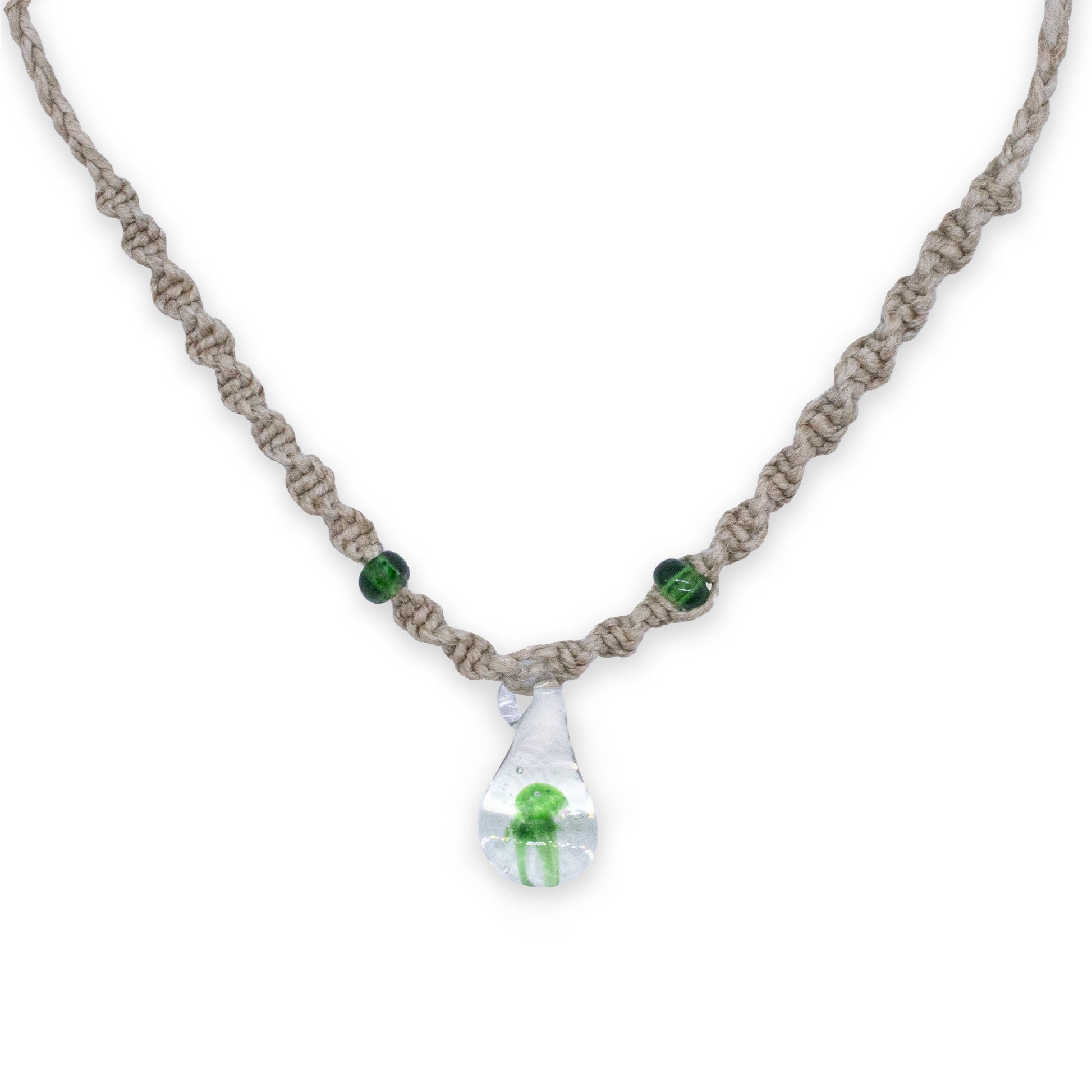 A handmade macrame necklace with a clear teardrop pendant containing a small green mushroom frog, accented with two green beads on a white background.