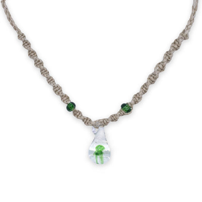 A handmade macrame necklace with a clear teardrop pendant containing a small green mushroom frog, accented with two green beads on a white background.