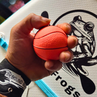Hand holding a small orange basketball with a Rebound bungy and wrist strap. on a white Paddle Frogs background