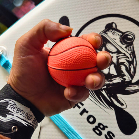 Hand holding a small orange basketball with a Rebound bungy and wrist strap. on a white Paddle Frogs background
