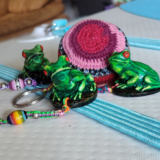 Green frog figurines with colorful keychains on a textured surface